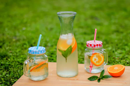 Fresh aromatic orange and mint water in glass and jarの写真素材