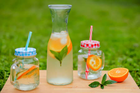 Fresh aromatic orange and mint water in glass jar served on a wooden tableの写真素材