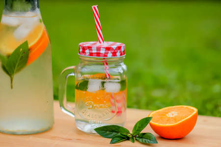 Fresh aromatic orange and mint water in glass jar served on a wooden tableの写真素材
