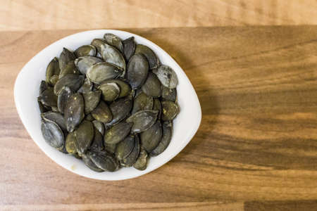 Pumpkin seeds in a bowl on a wooden background closeup