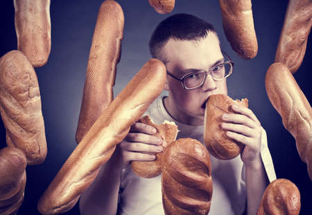 The young man wearing spectacles eats a long loafの写真素材