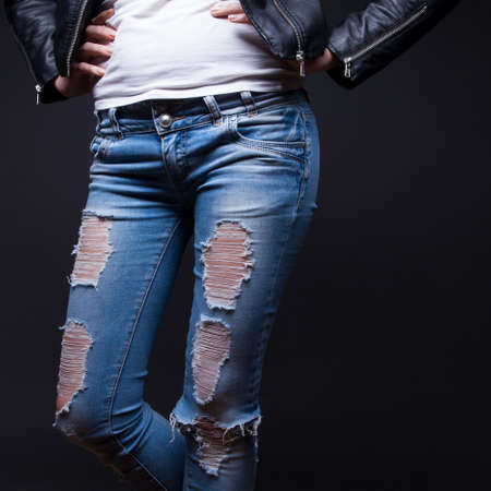 Women's legs in ragged jeans on a black background