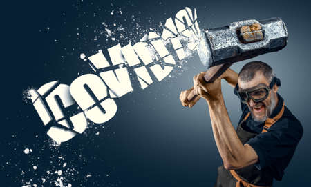 The man breaks the text with a sledgehammer. The word covid shatters into piecesの写真素材