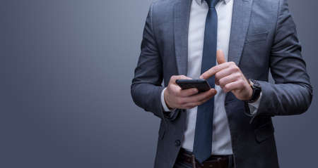 Business man scrolls the tape on the smartphone. Gray background.の写真素材