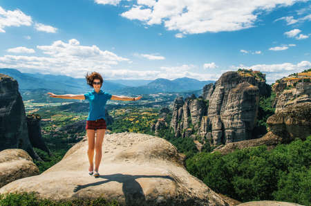 Young happy woman stands back to the rock with raised hands. Traveler enjoying the landscape with mountain, Monasteries of Meteora, Greeceの写真素材