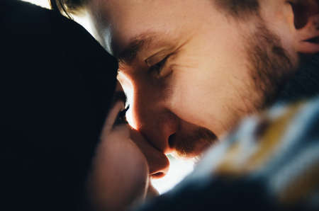 Happy girl in a hat kissing and touches noses boyfriend with a red beard and looking to his eyes. Happy moments. Close up portraitの写真素材