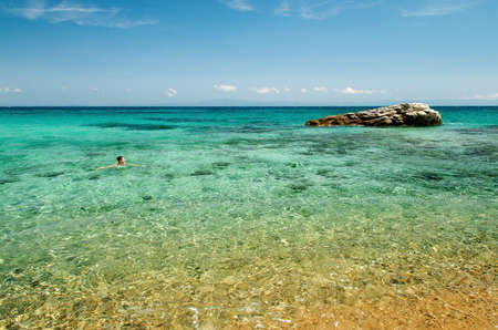 Young woman swims in the azure blue sea against the big stone.の写真素材