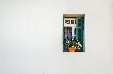 View of the white stone house and the small green window with the curtains and small pot of colorful...