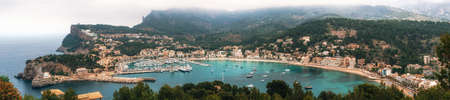 Panoramic view of Port de Soller with harbour, yachts, tourist boats, colorful architecture and beach on a cloudy day. Landmark of Mallorca, Spainの写真素材