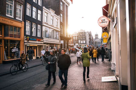 Amsterdam, Netherlands - 25 April, 2017: Tourist walk along a narrow street of the historical town part of Amsterdam at sunset.のeditorial素材
