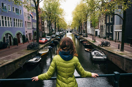 Young woman stands on the bridge and looks at the canal of Amsterdam, Netherlandsの写真素材