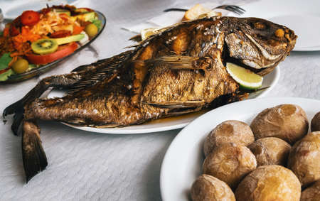 Grilled fish on plate, canarian wrinkly potatoes and salad with vegetables and fruits. Tenerife,...