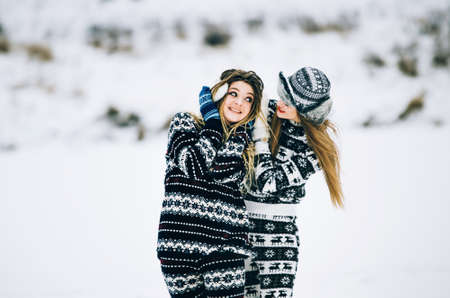 Couple of young woman. Girl wears warm hat girl closes friend's ears with her hands in mittens in cold winterの写真素材