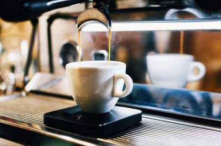 Professional espresso machine pouring fresh coffee into white ceramic cup with reflection on backgroundの写真素材