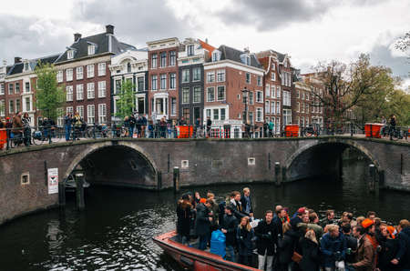Amsterdam, Netherlands - 25 April, 2017: Local people and tourists ride on boats under narrow bridges and participate in celebrating King's Day along the canal and promenade of Amsterdam.のeditorial素材