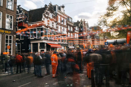 Amsterdam, Netherlands - 27 April, 2017: Streets of Amsterdam full of people in orange during the celebration of kings day. Blurred people at sunset with sunlight and orange decorations.のeditorial素材