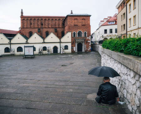 Krakow, Poland - May 23, 2017: Adult man sits with umbrella against old Synagogue in the historic Kazimierz, old jewish district in Krakow, Polandのeditorial素材