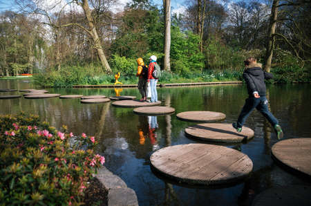 Keukenhof, Lisse, Netherlands - April 26, 2017: Boy cross stone steps through pond with tourists on sunny spring dayのeditorial素材