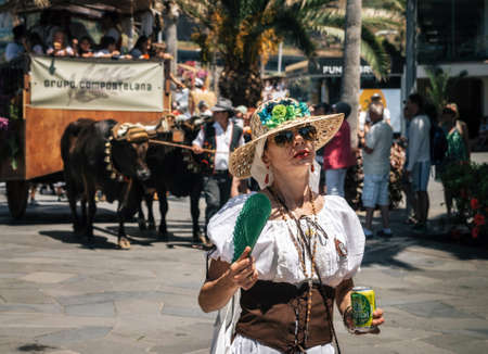 Puerto de la Cruz, Tenerife, Canary Islands, Spain - May 30, 2017: Expressive woman with fan in traditional clothes against decorated bull drawn wagon. Tenerife celebrate the Day of the Canary Islands.のeditorial素材