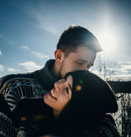 Joyful cute couple embraces. Young man in a sweater hugs a girl and kisses her in winter. The concept of a successful relationship and happy momentsの写真素材