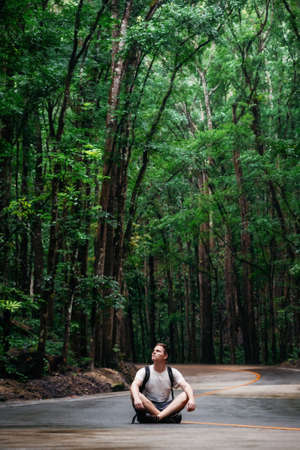 Man with backpack sits on road through green Bilar Man-Made Forest, Bohol, Philippinesの写真素材