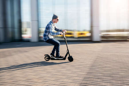 Young man in casual wear on electric kick scooter on city street in motion blur in sunday