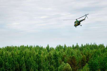 Khaki colored helicopter is flying in blue sky above forestの写真素材