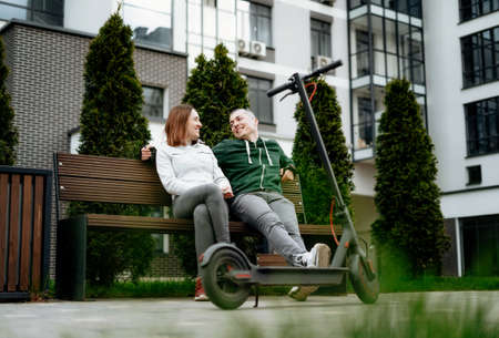 Couple sit next to electric kick scooter in street and laughing.の写真素材