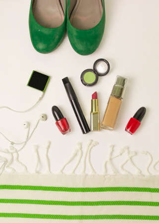 preparation of a woman for the holiday in red and green colors - on the table a tone cream, lipstick, mascara, lip gloss, beige shadows, red nail polish. flatlay. filming on top. green shoes. white and green fabric, striped fabricの写真素材