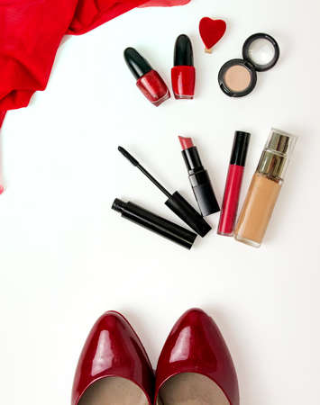 preparation of a woman for the holiday - on the table a tone cream, lipstick, mascara, lip gloss, beige shadows, red nail polish. flatlay. red shoesの写真素材