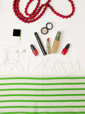 preparation of a woman for the holiday in red and green colors - on the table a tone cream, lipstick, mascara, lip gloss, beige shadows, red nail polish. flatlay. filming on top. green shoes. white and green fabric, striped fabricの写真素材