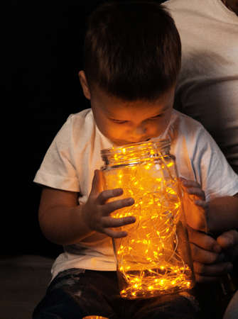 little boy sitting on the floor with dad and looking in a jar with a garland, yellow light. joy. happiness. new Year. Christmasの写真素材