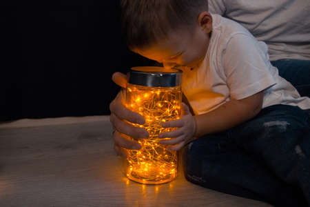 little boy sitting on the floor with dad and looking in a jar with a garland, yellow light. joy. happiness. new Year. Christmasの写真素材