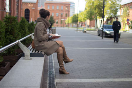 young woman sitting on a bench with a book in her hands, looking awayの写真素材