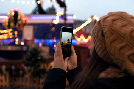 the girl at the Christmas market takes a picture of the carousel on the phone. new Year. Christmas. Europeの写真素材