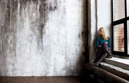 a young woman sits on a windowsill and looking in the room