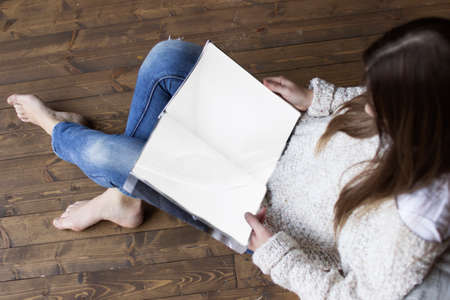 brunette girl sits on a wooden floor and reads a book, top viewの写真素材