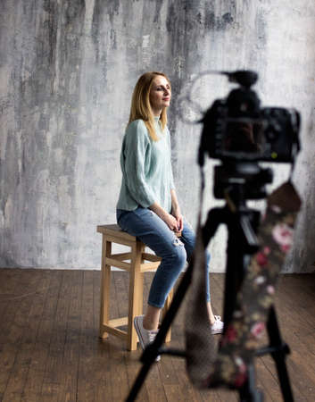 backstage with professional shooting in the studio, the model sits on a chair, a professional camera in the defocusの写真素材