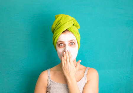 young woman with a turban of green towels with a white mask on her face holds hand near the mouth and is very surprised on a blue background, popart womanの写真素材
