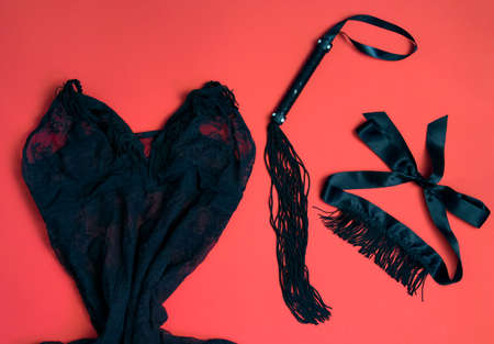 Women's things for a romantic evening - lacy black underwear, black whip, eye patch with fringe on a red background. Valentine's Day. love and passionの写真素材