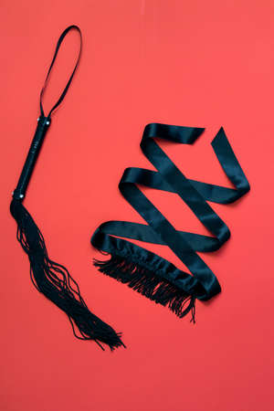 Women's things for a romantic evening - lacy black underwear, black whip, eye patch with fringe on a red background. Valentine's Day. love and passionの写真素材