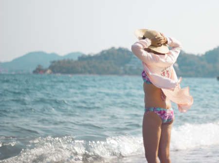 a young girl in a pale pink shirt and a straw hat stay near the sea. Holidays. Recreation. The sun. Ocean. Sea. Shooting from the backの写真素材