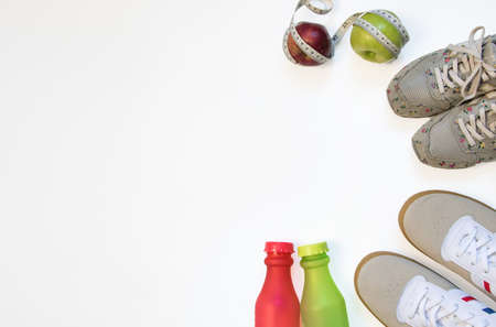 Sports accessories for two are top view. men's and women's sneakers, green sports bottle, red sports bottle, red apple and green apple, obfuscated with a measuring tape on a white background.の写真素材