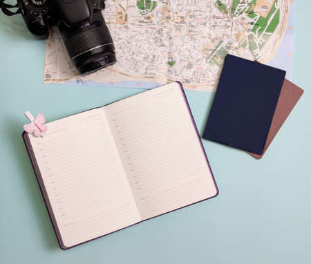 Travel items flatlay. on a blue background - a map, a camera, a notebook and a passport.