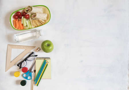 A pile of various stationery on table, notepad, colored pencils, ruler, marker, planer, space for text. Delicious school lunch box, sandwich and fruit. The concept of preparing childrenの写真素材