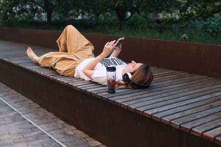 Teenage female listening music outdoor, lying on bench and relaxingの写真素材