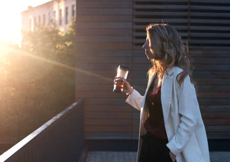 Rear view of businesswoman look at sunrise above city with cup of teaの写真素材
