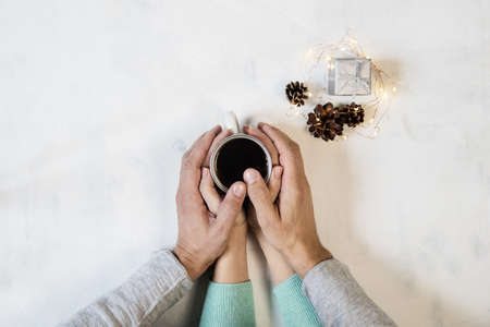 Couple in love holding hands with coffee on white marble table, with christmas lights. Photograph taken from above, top view with copy spaceの写真素材