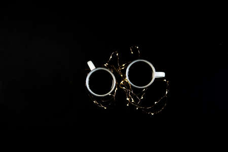 Two cups with coffee on black table with christmas lights. Photograph taken from above, top view with copy space.の写真素材