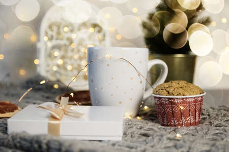 Winter still life from scarf, white mug of cocoa, coffee or hot chocolate, muffin, christmas tree on warm plaid with garland.の写真素材